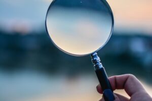 A magnifying glass held by a hand outdoors at sunset, focusing on exploration.