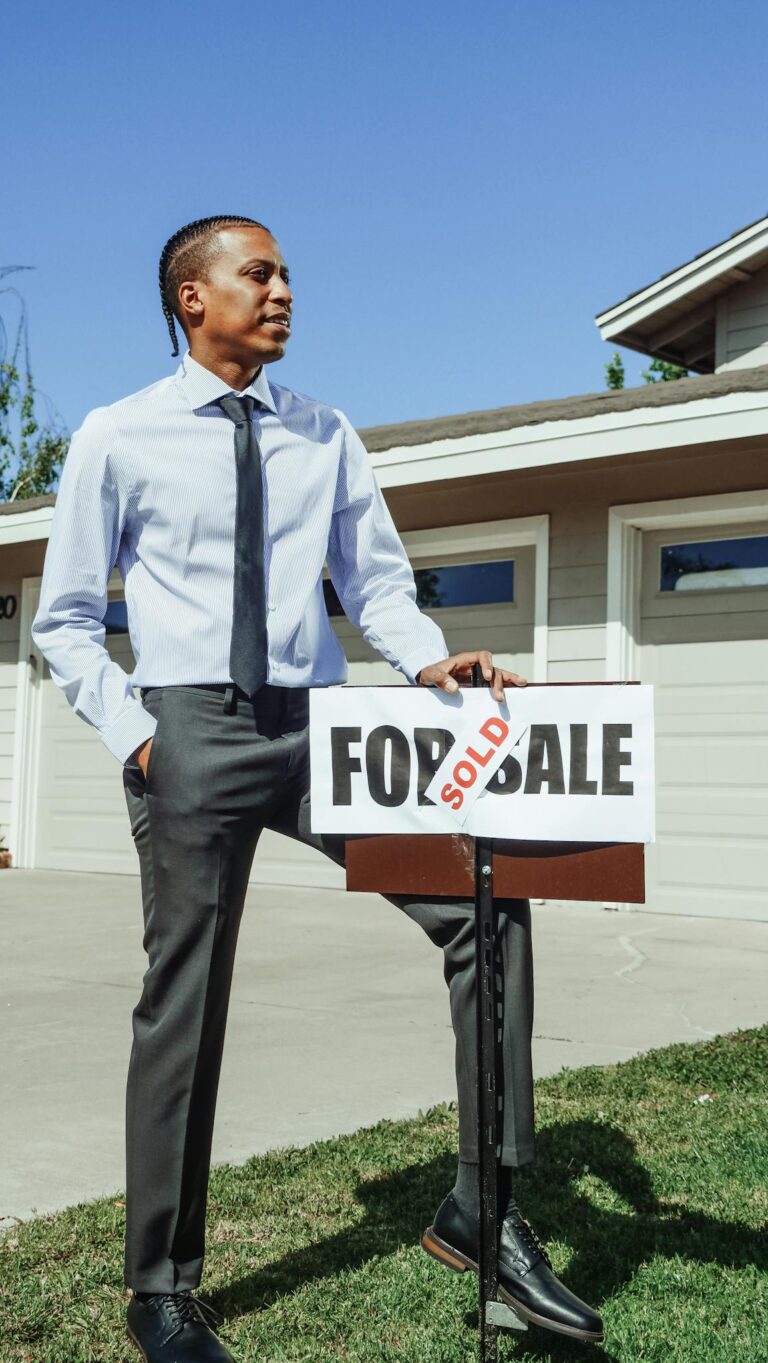Realtor standing beside a sold sign in front of a new home.